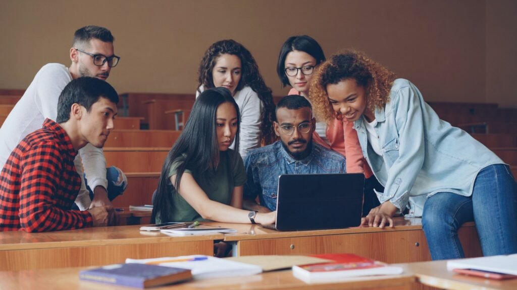A diverse group of students gathered around a laptop